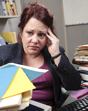 Person surrounded by stacks of files, looking stressed.