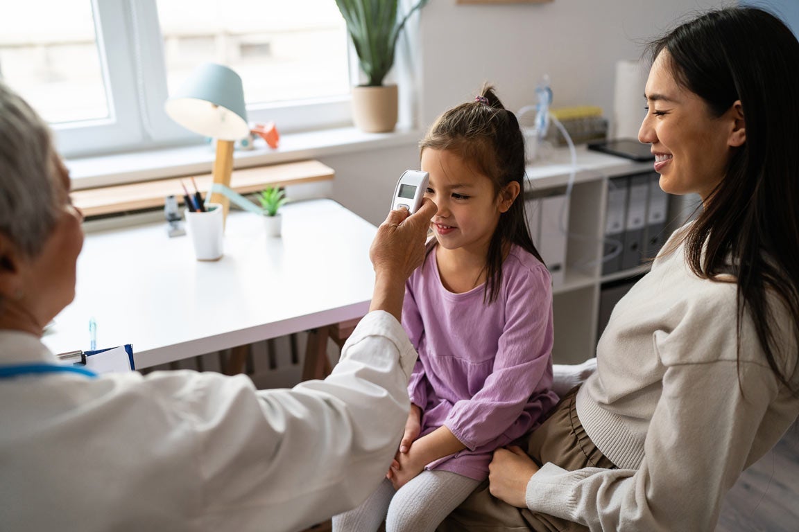 Daughter on mother's lap getting temperature taken at doctor's office 