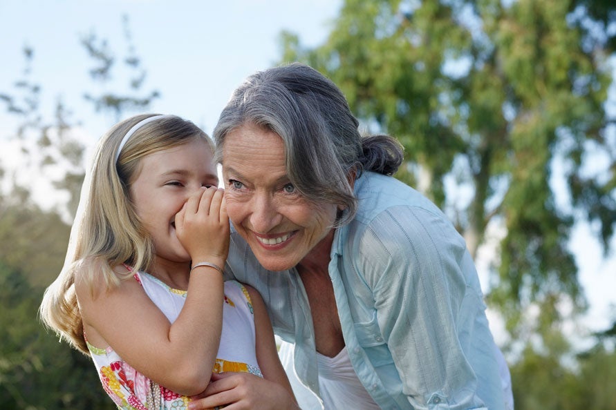 Granddaughter whispering to grandmother's ear outdoors