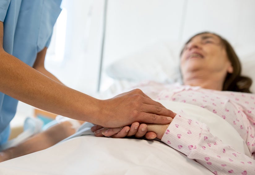 Close-up on a nurse holding the hand of a sick woman in bed